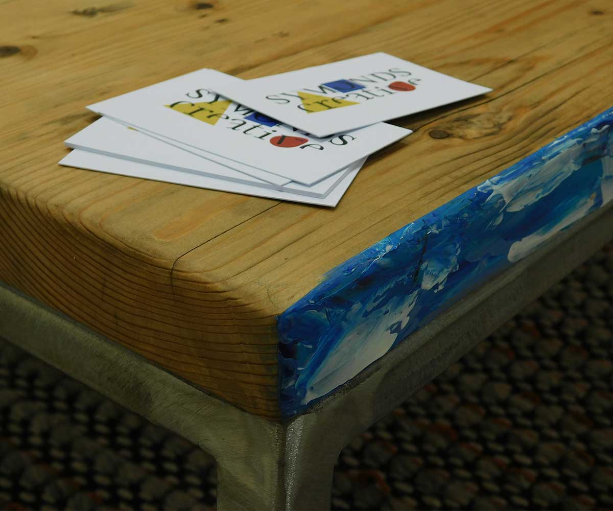 A close-up detail of one of Symonds Creative’s early tables. It has a blue, painted edge with Symonds Creative business cards on top of it.